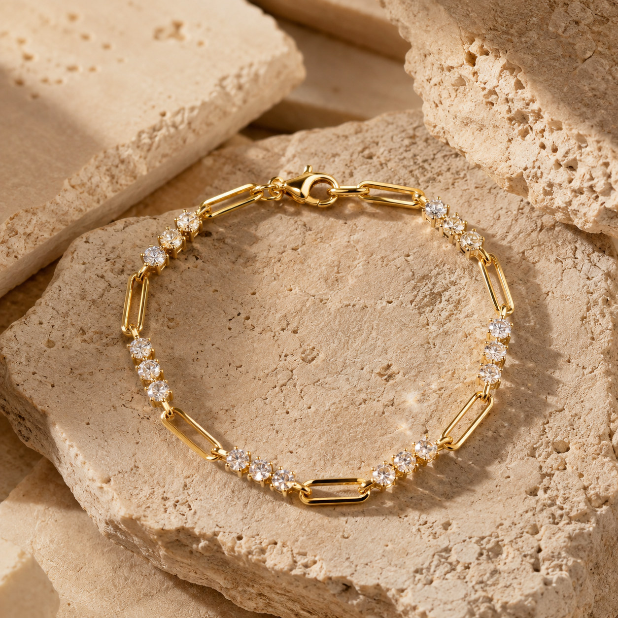 Gold-toned link bracelet set with clear stones on textured beige stone forms.