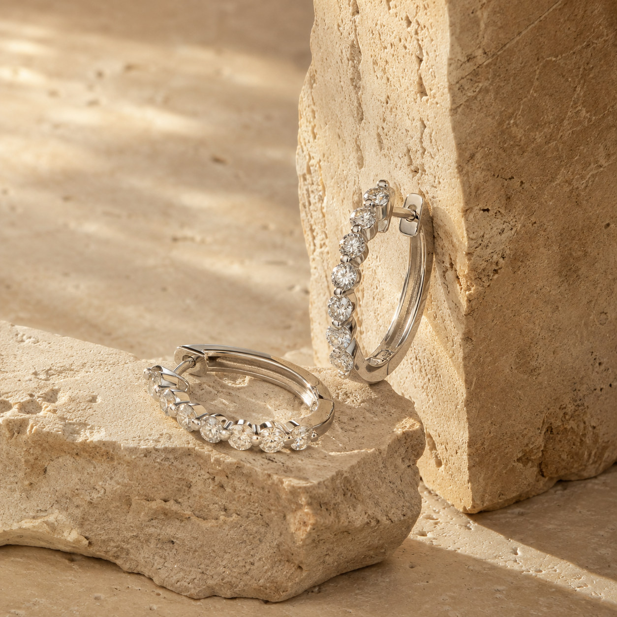 Pair of silver-toned hoop earrings set with clear stones on textured beige stone forms.