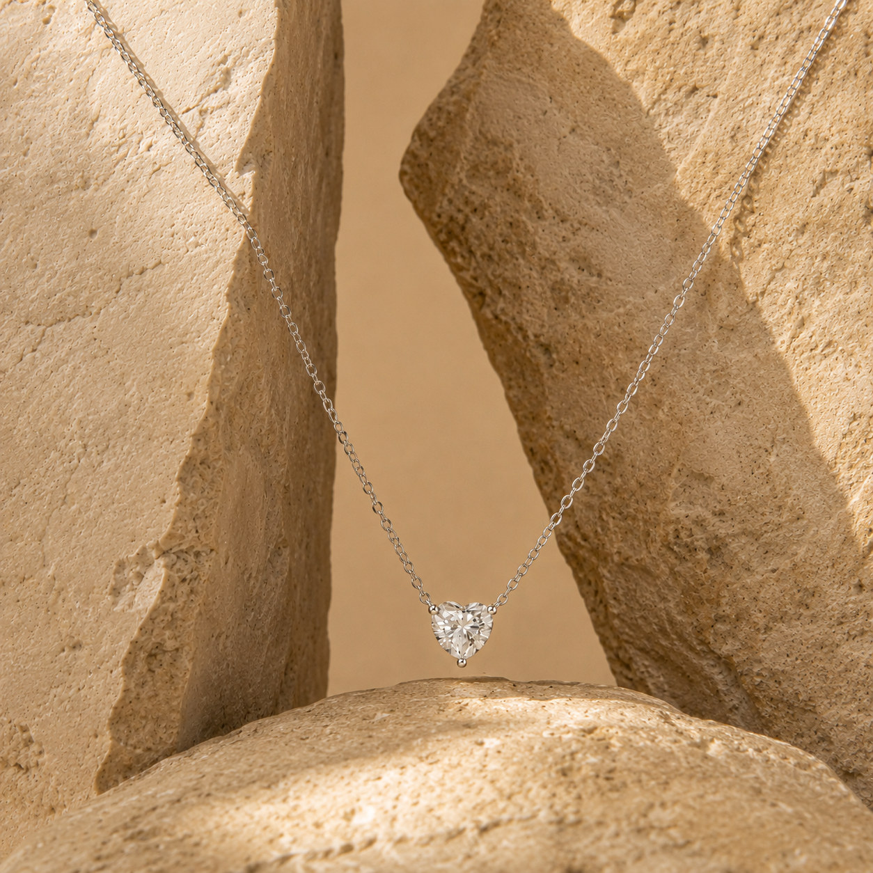 Heart-shaped pendant on a fine chain suspended between textured beige stone forms.